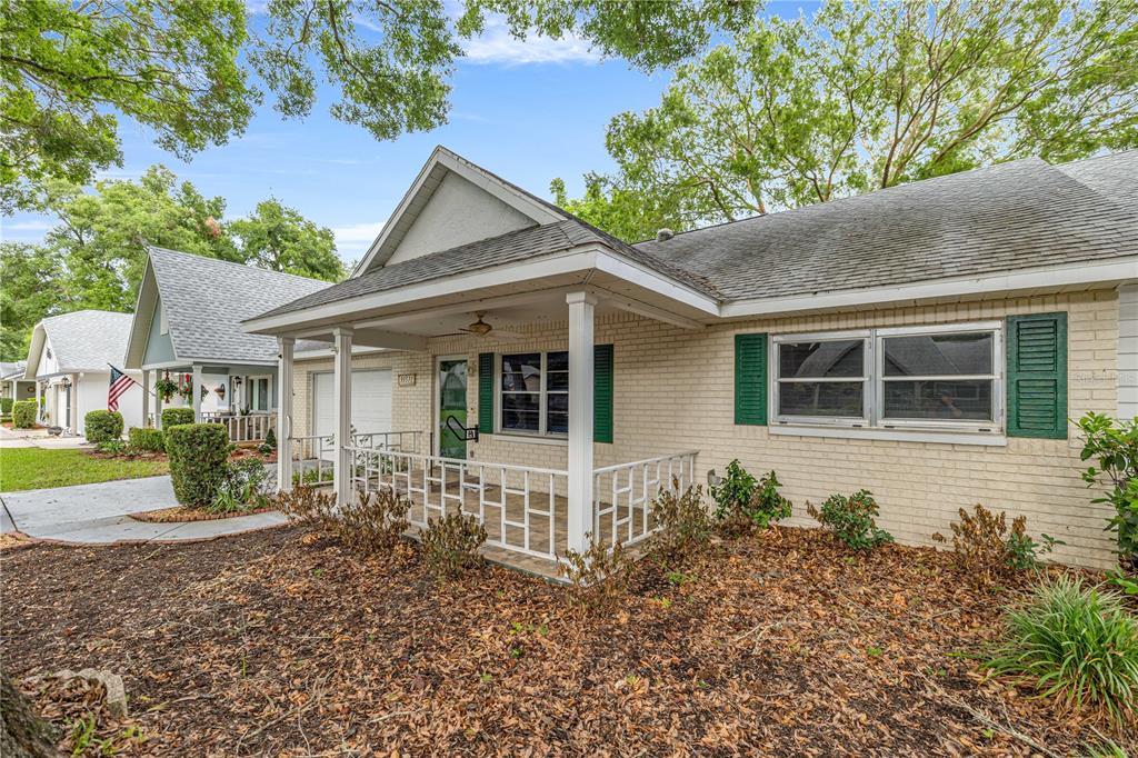A single-story brick house with a covered front porch and green shutters under mature trees — 9357 SW 82ND TERRACE UNIT C, OCALA, FL