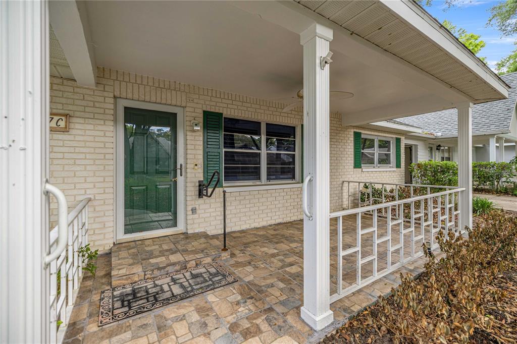 A covered front porch with tiled flooring, white railings, and a brick exterior wall — 9357 SW 82ND TERRACE UNIT C, OCALA, FL