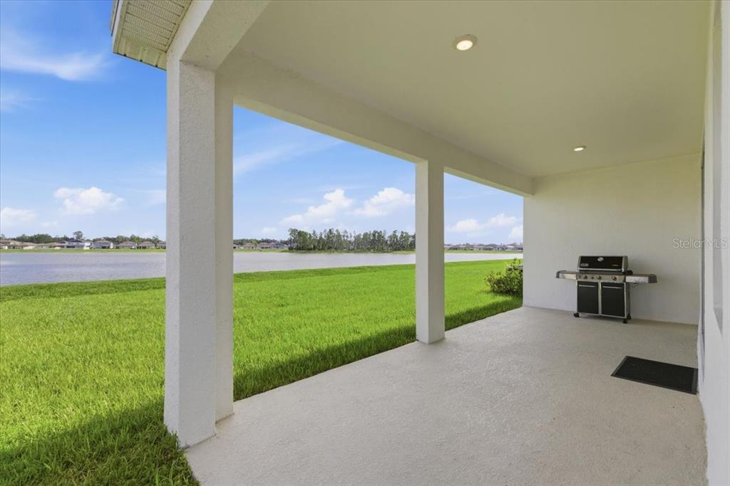A covered concrete patio overlooks a grassy lawn and a lake under a blue sky — 1413 TROPICAL OASIS AVENUE, PLANT CITY, FL