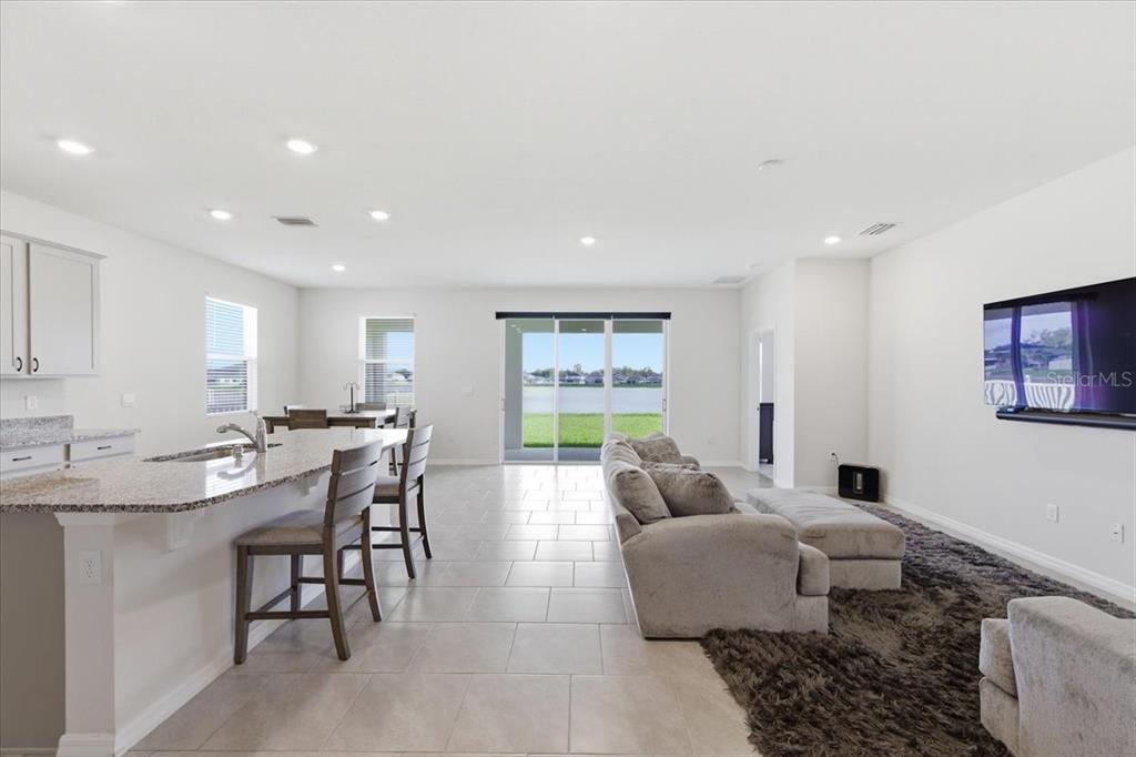 An open-concept kitchen and living room with tile floors, granite countertops, and a lake view — 1413 TROPICAL OASIS AVENUE, PLANT CITY, FL