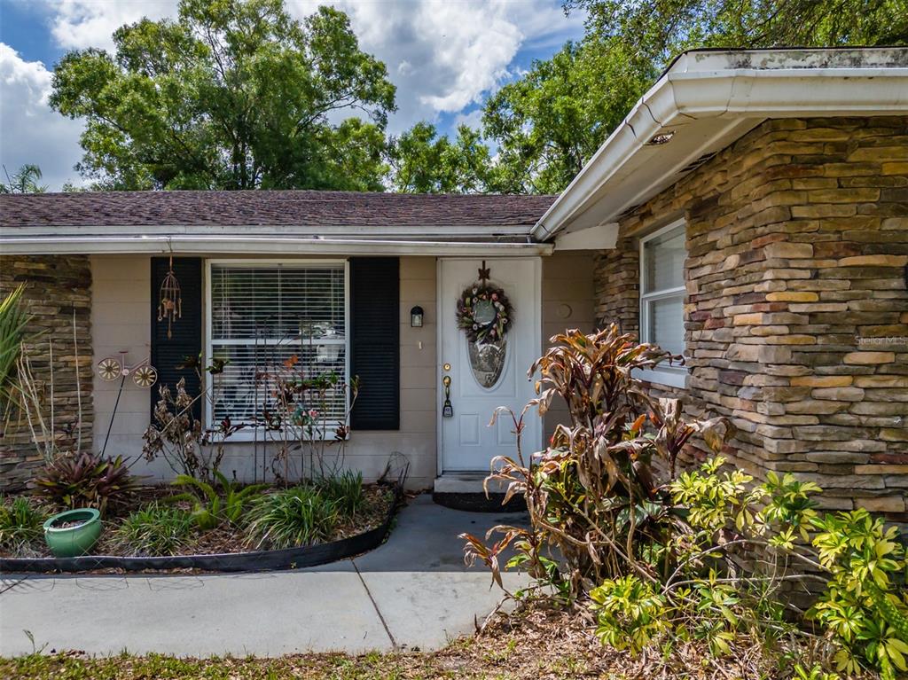 The exterior of a house features a stone facade, a white front door, and landscaping — 18853 TRACER DRIVE, LUTZ, FL