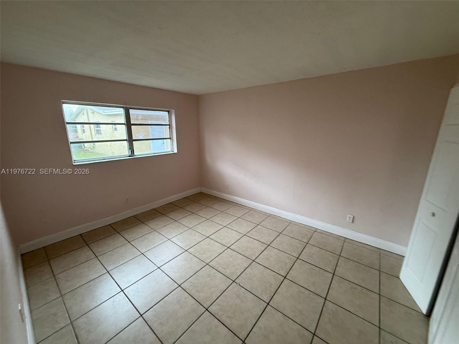 An empty room features light pink walls, beige tile flooring, and a single window — 4732 SW 33rd Ave # 103, Dania Beach FL 33312, DANIA BEACH, FL