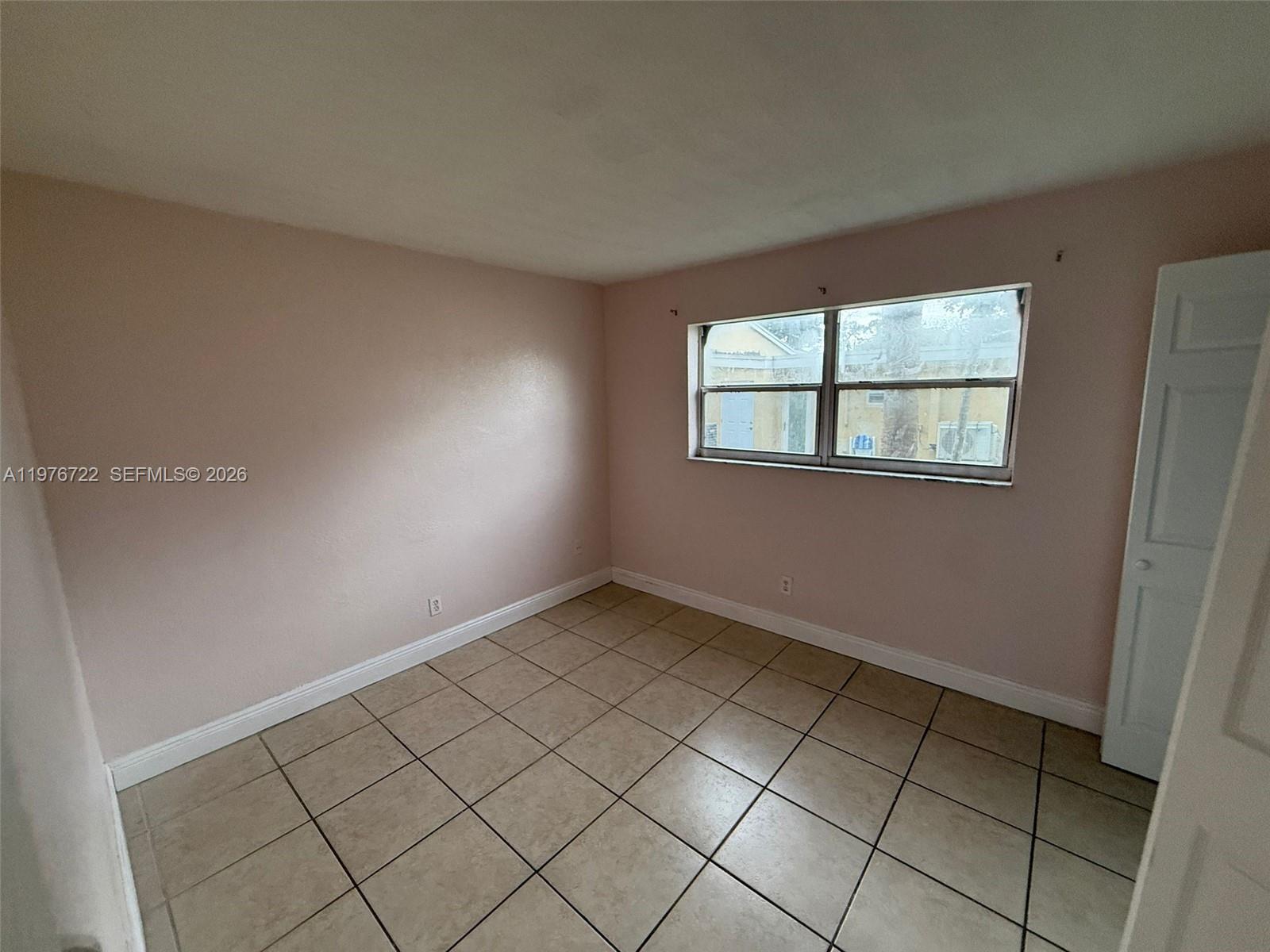 An empty bedroom features light pink walls, beige tile flooring, and a single window — 4732 SW 33rd Ave # 103, Dania Beach FL 33312, DANIA BEACH, FL