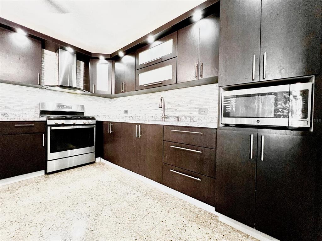 A modern kitchen features dark wood cabinets, stainless steel appliances, and a speckled tile floor — J39 URB.VILLA ANDALUCIA CALLE GAUCIN, SAN JUAN, PR