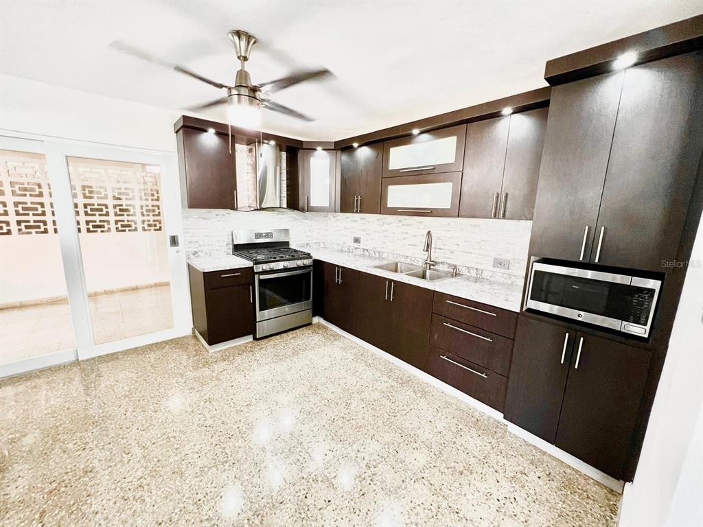 A modern kitchen features dark wood cabinets, stainless steel appliances, and speckled stone flooring — J39 URB.VILLA ANDALUCIA CALLE GAUCIN, SAN JUAN, PR