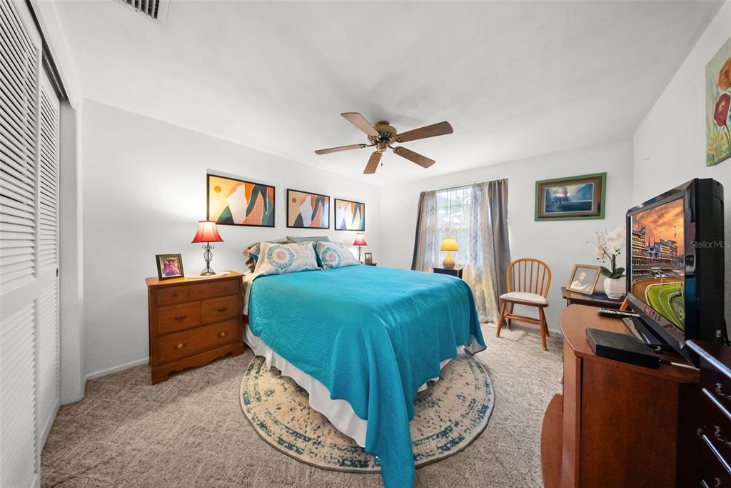A bedroom features a bed with a blue quilt, a ceiling fan, and carpeted flooring — 4227 RAX PLACE UNIT 4227, NEW PORT RICHEY, FL