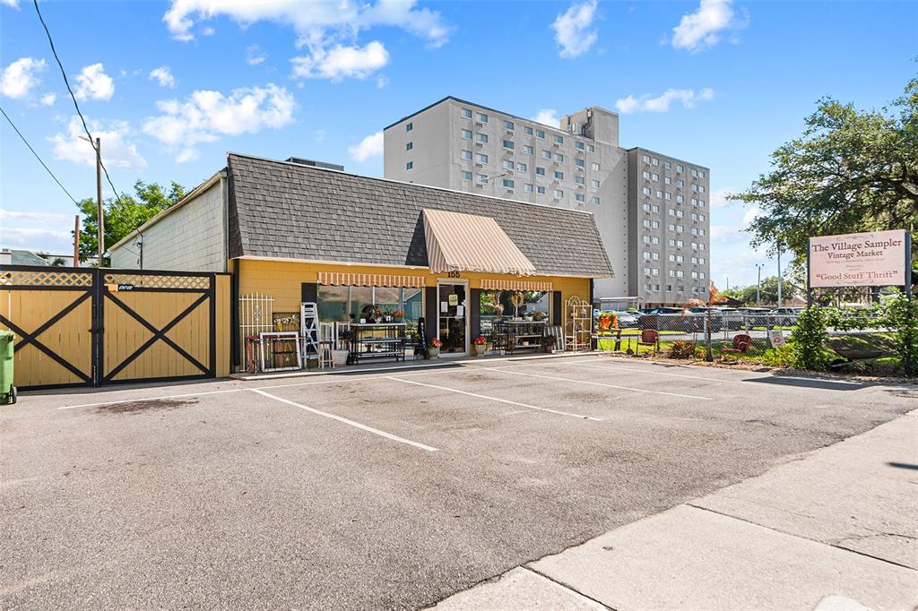 A yellow, single-story retail building with a parking lot and a tall apartment complex behind — 155 AVENUE B SW, WINTER HAVEN, FL