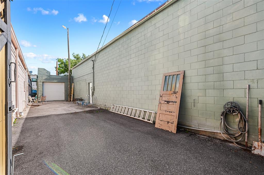 An outdoor alleyway features a long, light green concrete block wall, a ladder, and a door — 155 AVENUE B SW, WINTER HAVEN, FL