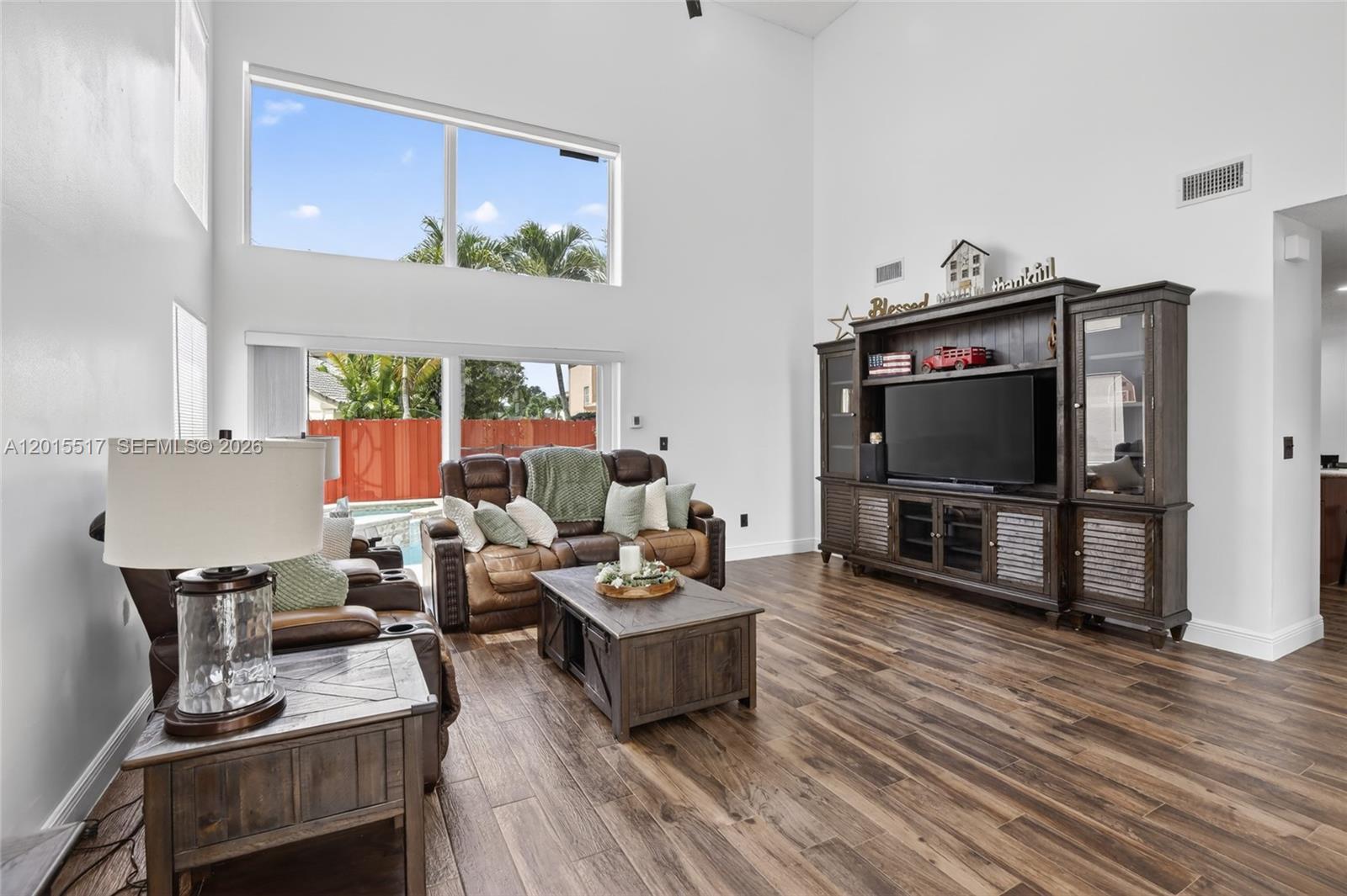 A living room features high ceilings, wood-look tile floors, and a large entertainment center — 14630 Cedar Creek Pl, Davie FL 33325, DAVIE, FL