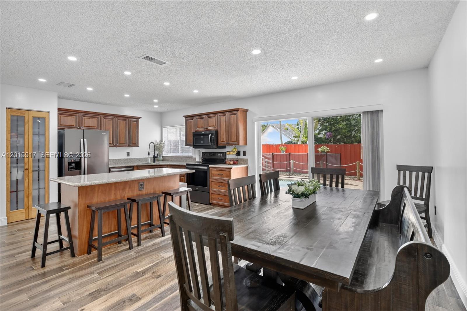 A kitchen with wood cabinets and a granite island opens to a dining area — 14630 Cedar Creek Pl, Davie FL 33325, DAVIE, FL