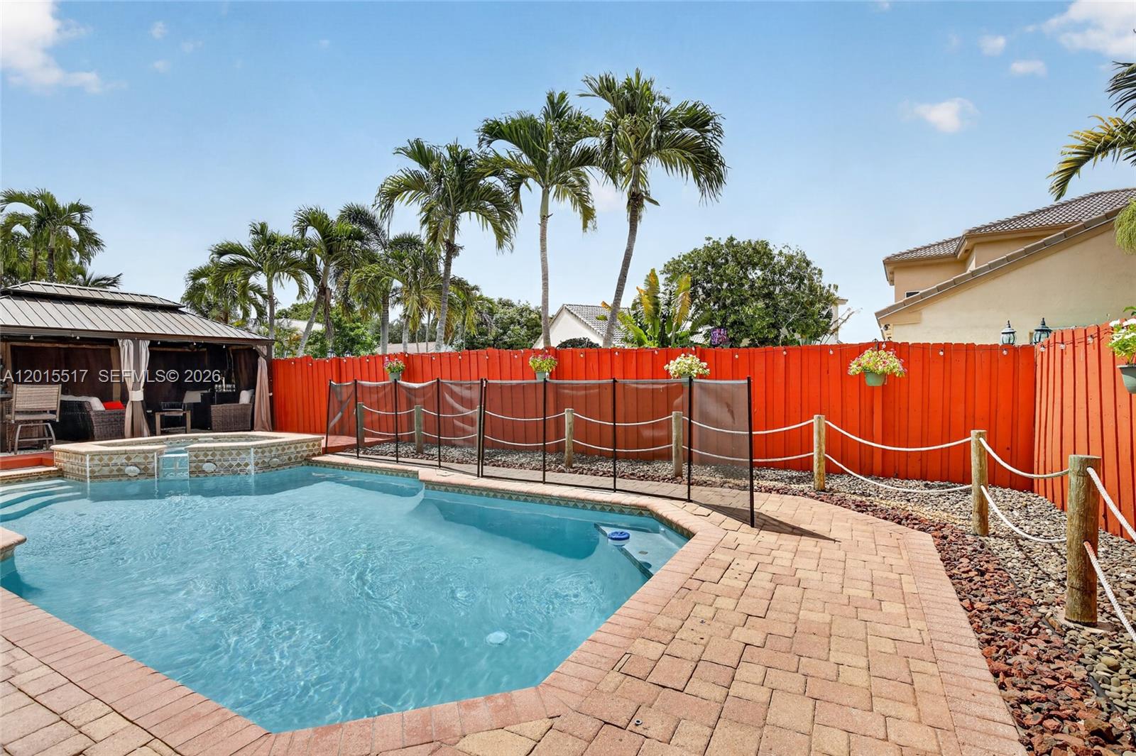 A swimming pool with a safety fence sits in a backyard with a red fence — 14630 Cedar Creek Pl, Davie FL 33325, DAVIE, FL