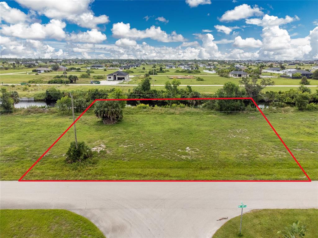 An aerial view shows a vacant, rectangular grassy lot bordered by a canal and road — 3902 NW 41ST LANE, CAPE CORAL, FL