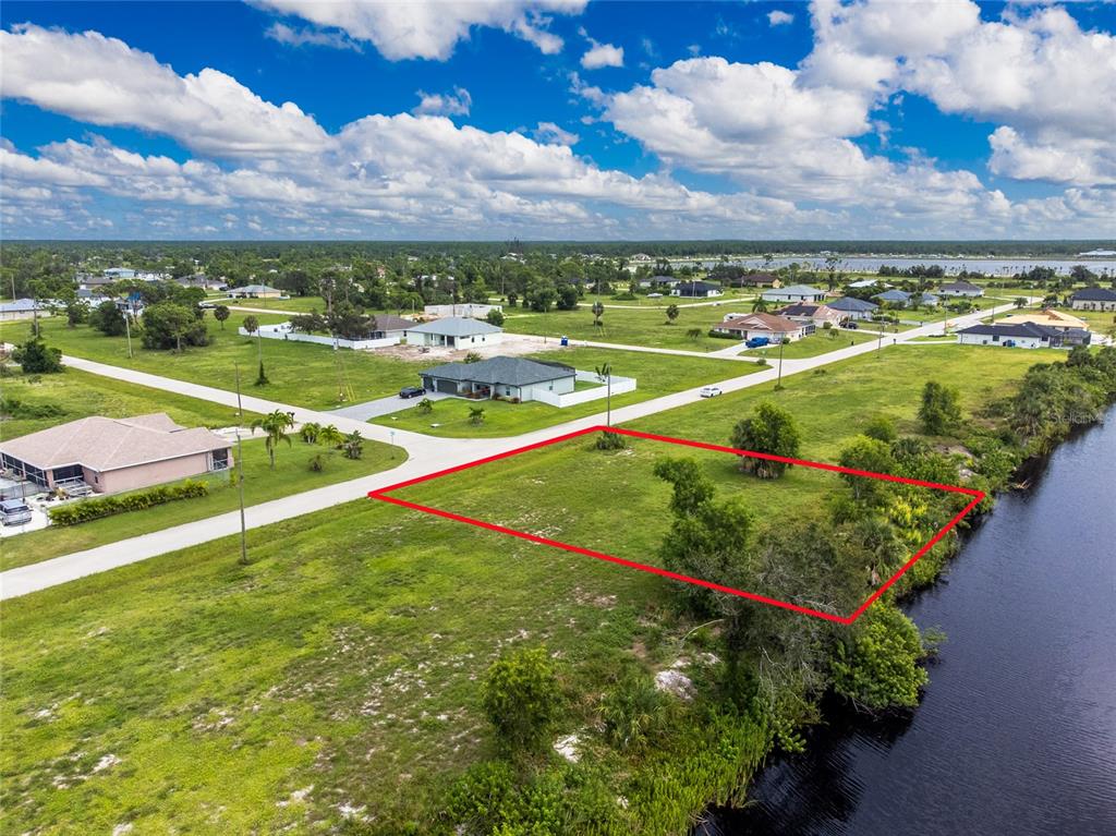 An aerial view shows a vacant, rectangular waterfront lot outlined in red near a road — 3902 NW 41ST LANE, CAPE CORAL, FL