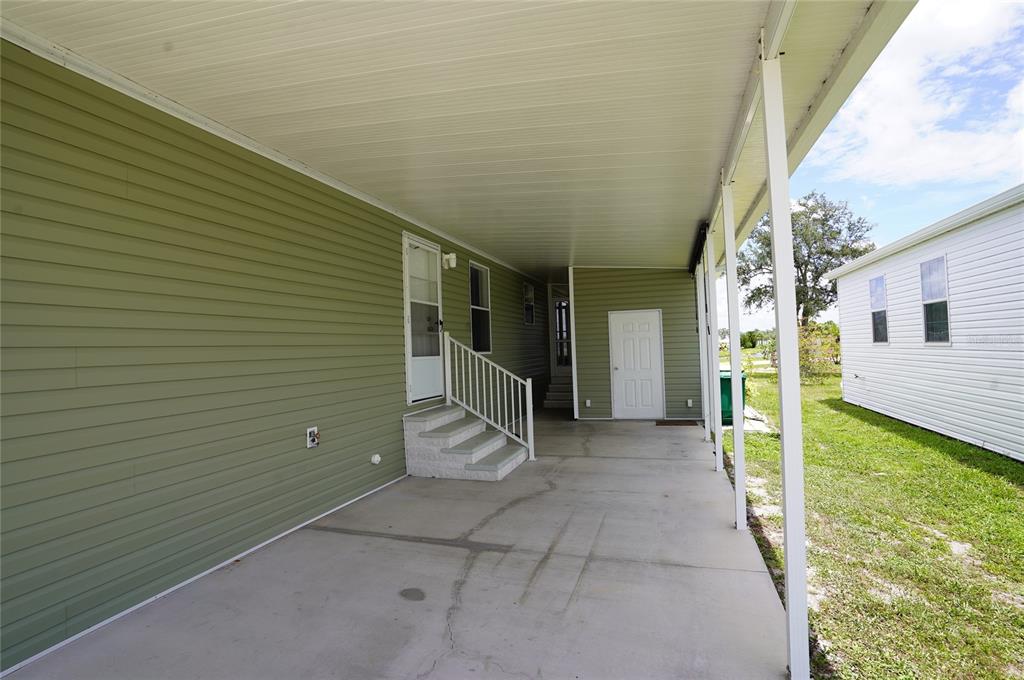 A covered concrete carport sits beside a green-sided mobile home with white stairs — 14510 COSTINE COURT, PORT CHARLOTTE, FL