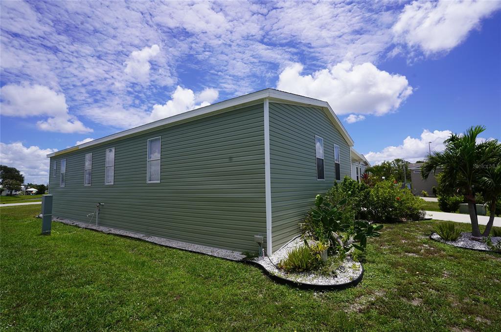 The exterior of a green mobile home with white trim sits on a grassy lot — 14510 COSTINE COURT, PORT CHARLOTTE, FL
