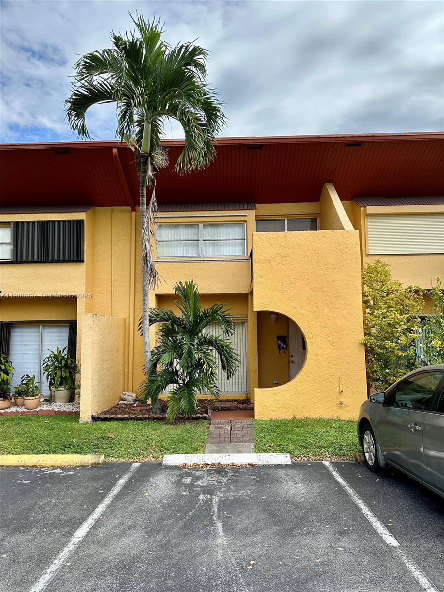 A two-story yellow townhouse features a palm tree in front and a reserved parking space — 13705 SW 84th St # F, Miami FL 33183, MIAMI, FL