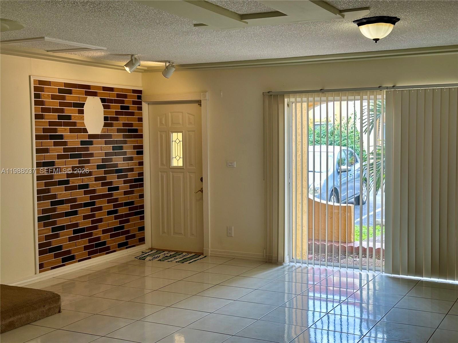 A room with tiled floors, a brick accent wall, a front door, and sliding glass doors — 13705 SW 84th St # F, Miami FL 33183, MIAMI, FL