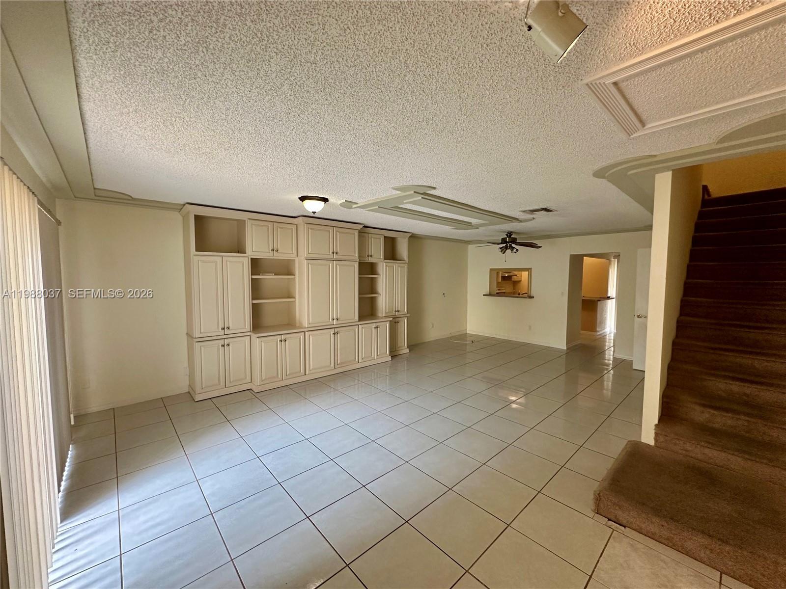 A living room features large white built-in cabinets, tile flooring, and a carpeted staircase — 13705 SW 84th St # F, Miami FL 33183, MIAMI, FL