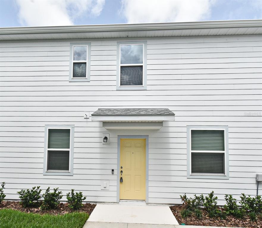 A two-story house exterior features white horizontal siding, a yellow front door, and a small porch — 3101 EMERALD ACRES LANE, SANFORD, FL