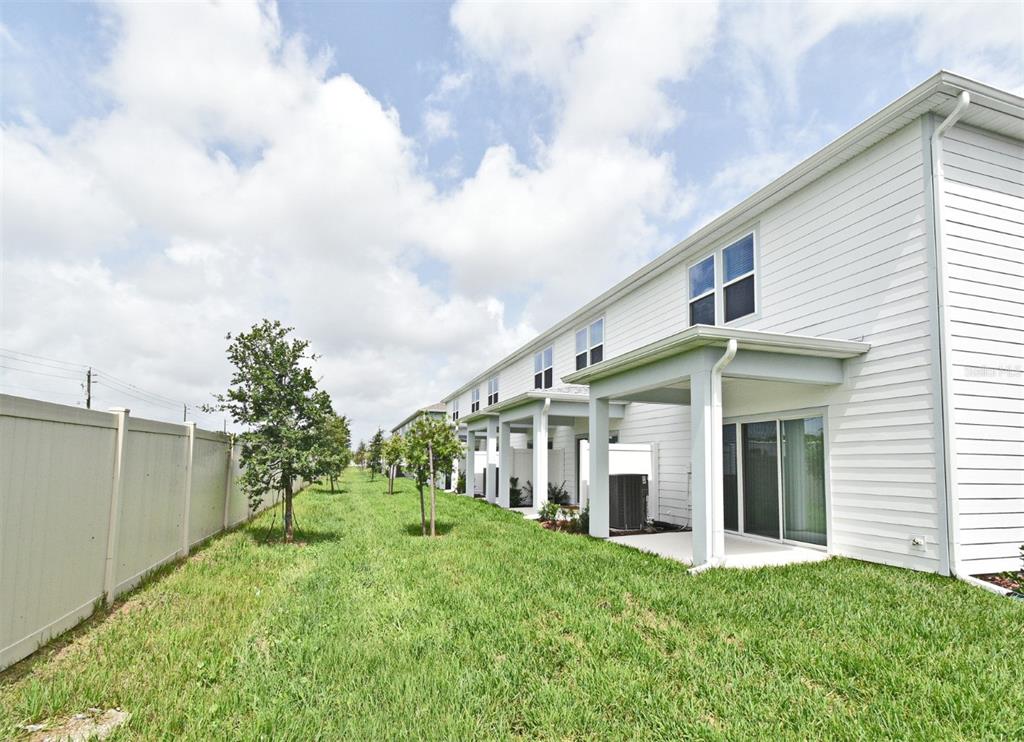 A white multi-unit townhouse exterior with a grassy yard and a vinyl privacy fence — 3101 EMERALD ACRES LANE, SANFORD, FL