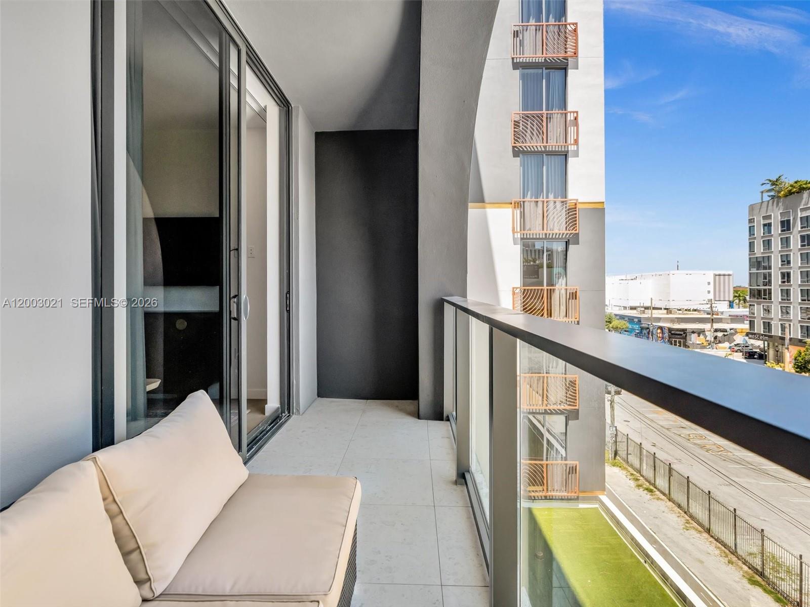 A balcony with a beige sofa, glass railing, and views of a neighboring building — 2700 NW 2nd Ave # 439, Miami FL 33127, MIAMI, FL