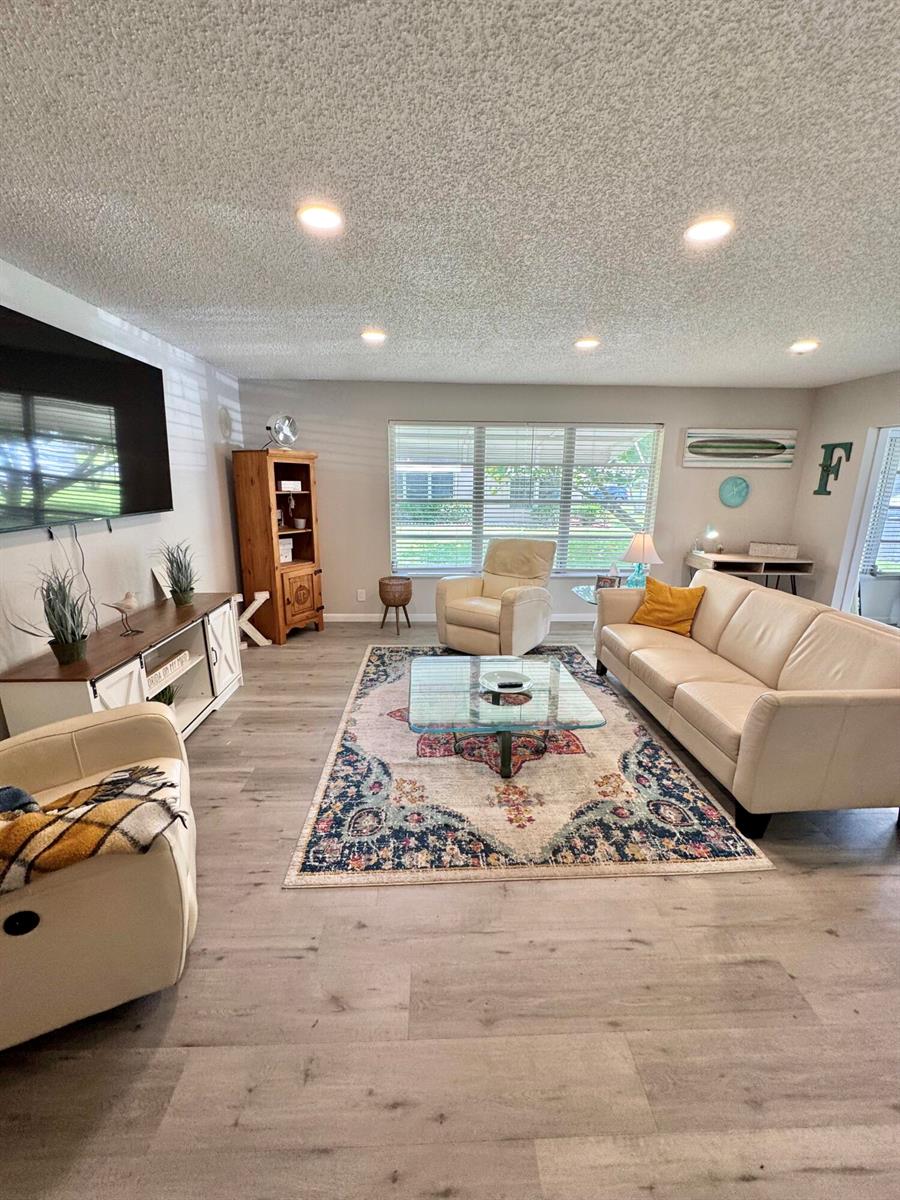 A living room with light wood floors, a beige sofa, two armchairs, and a patterned rug — 1342 High Point Way SE # D, Delray Beach FL 33445, DELRAY BEACH, FL