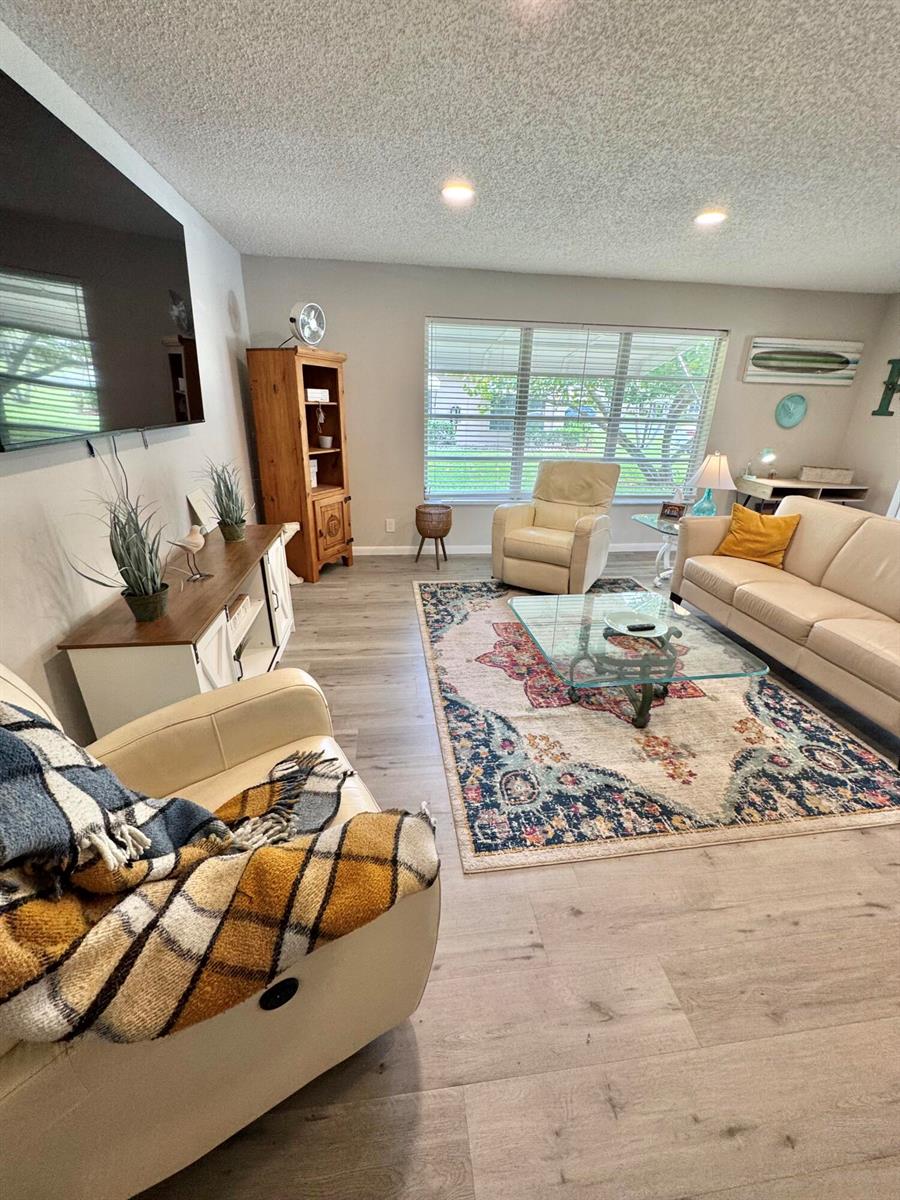 A living room features light wood-look flooring, a patterned area rug, and neutral-toned seating — 1342 High Point Way SE # D, Delray Beach FL 33445, DELRAY BEACH, FL