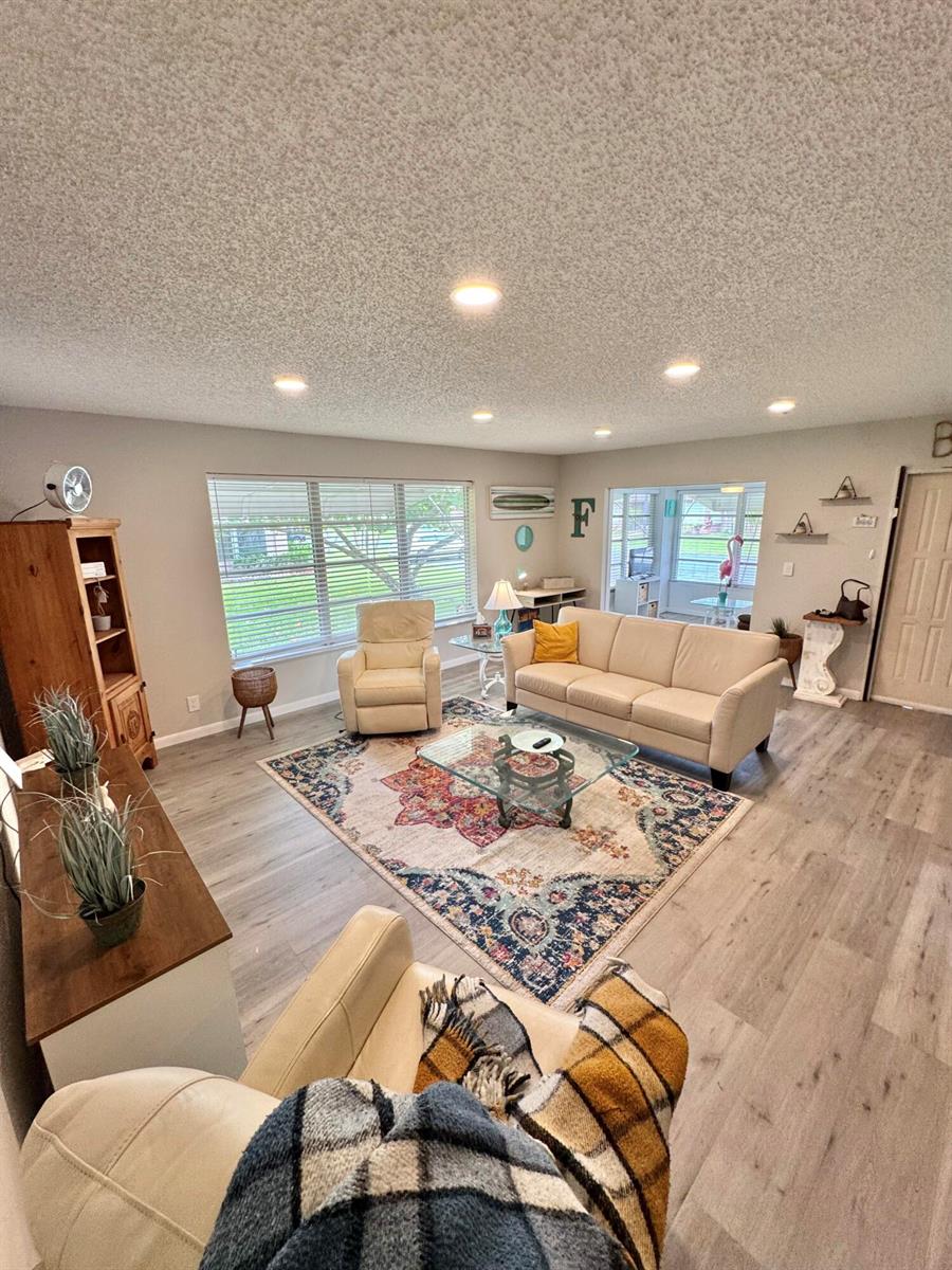 A living room features light wood-look flooring, a patterned area rug, and recessed ceiling lighting — 1342 High Point Way SE # D, Delray Beach FL 33445, DELRAY BEACH, FL