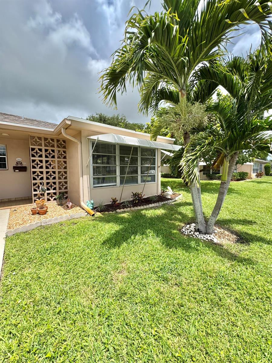 A tan house exterior features a decorative breeze block wall, metal window awning, and palm tree — 1342 High Point Way SE # D, Delray Beach FL 33445, DELRAY BEACH, FL