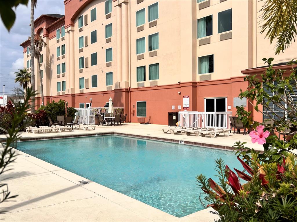 A rectangular swimming pool sits in front of a multi-story hotel building with tan walls — 3000 MAINGATE LANE UNIT 212, KISSIMMEE, FL
