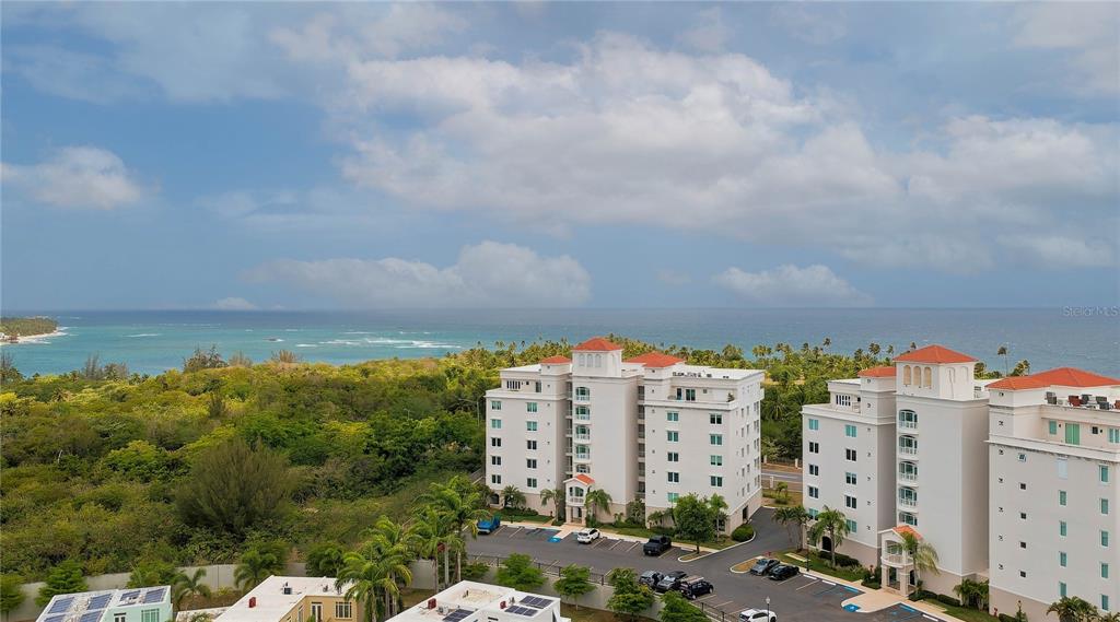 An aerial view shows multi-story white residential buildings near a lush green landscape and ocean — 145 OLIVINE STREET UNIT PH-571, VEGA ALTA, PR