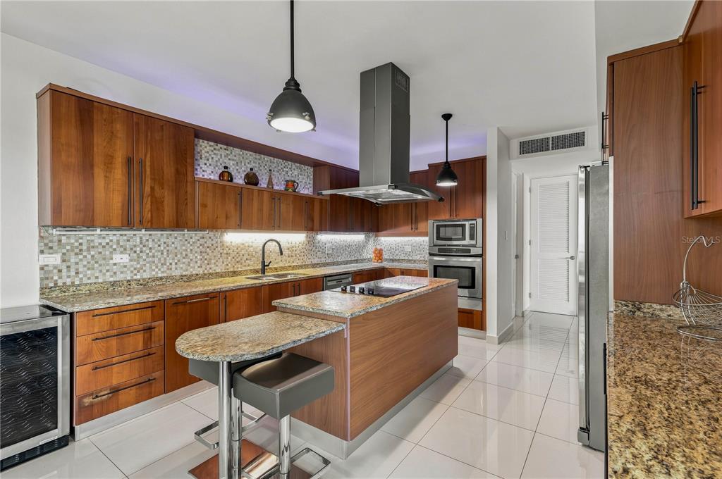 A modern kitchen features wood cabinetry, granite countertops, a central island, and stainless steel appliances — 145 OLIVINE STREET UNIT PH-571, VEGA ALTA, PR