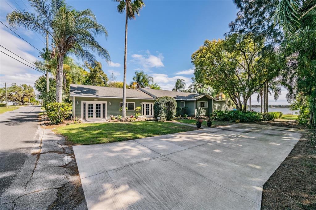 A single-story green house with a concrete driveway and palm trees sits near water — 1238 S HIGHLAND PARK DRIVE, LAKE WALES, FL