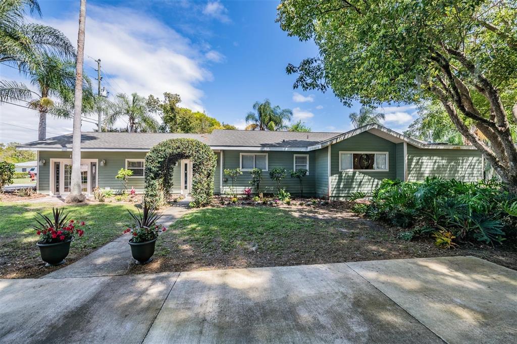 A single-story green house with a front garden, arched entryway, and a concrete driveway — 1238 S HIGHLAND PARK DRIVE, LAKE WALES, FL