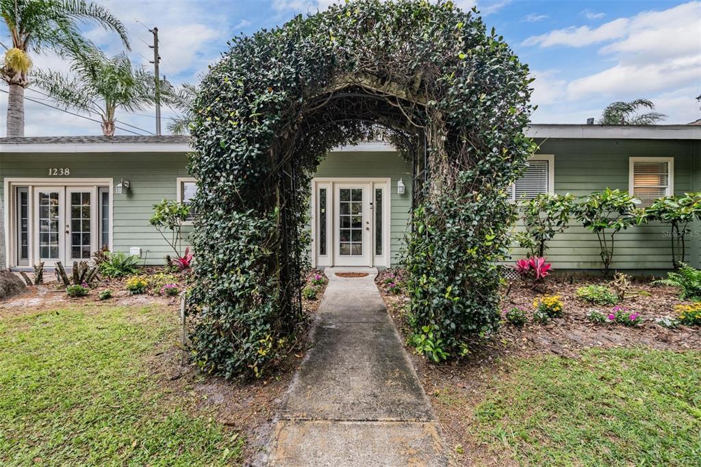 A green house exterior features a concrete walkway leading to a vine-covered metal archway — 1238 S HIGHLAND PARK DRIVE, LAKE WALES, FL