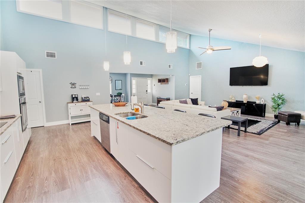 A modern open-concept kitchen and living area featuring a large granite-topped island and vaulted ceilings — 5417 PITCH PINE DRIVE, ORLANDO, FL