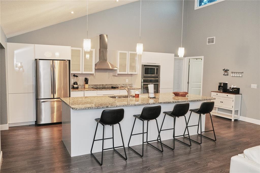 A modern kitchen features white cabinetry, a granite island with four stools, and stainless appliances — 5417 PITCH PINE DRIVE, ORLANDO, FL