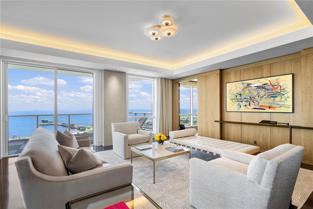 A modern living room features light-colored furniture, wood-paneled walls, and floor-to-ceiling windows overlooking the ocean — 400 BEACH DRIVE NE UNIT 2605, ST PETERSBURG, FL