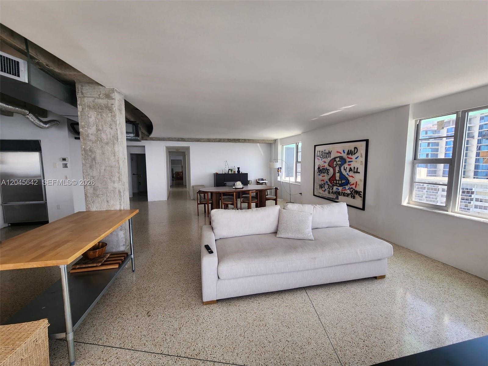 A spacious open-concept living and dining area features terrazzo floors, concrete columns, and modern furniture — 5255 Collins Ave # 12E, Miami Beach FL 33140, MIAMI BEACH, FL