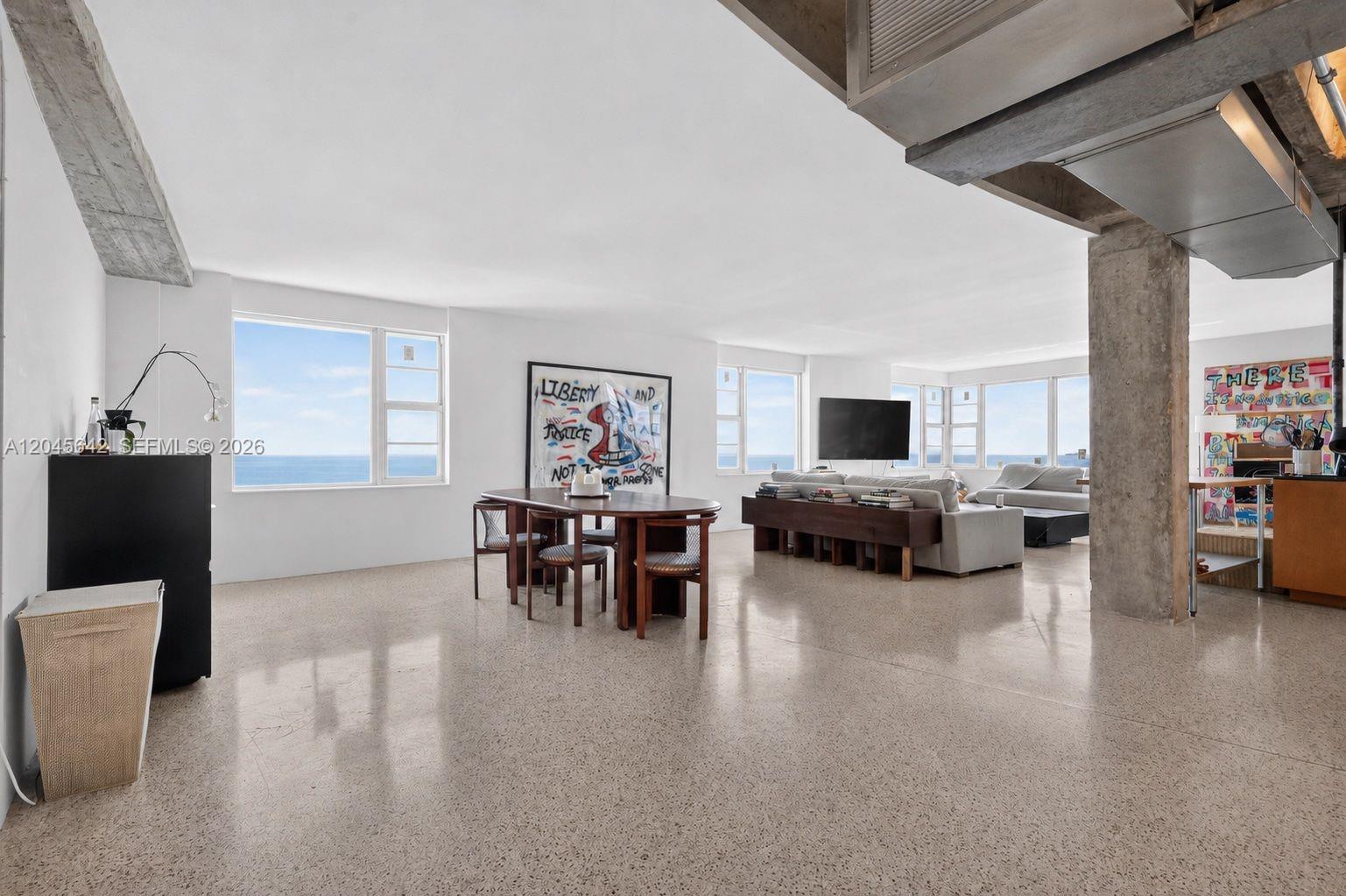 An open-concept living and dining area features concrete floors, exposed ceiling beams, and ocean views — 5255 Collins Ave # 12E, Miami Beach FL 33140, MIAMI BEACH, FL