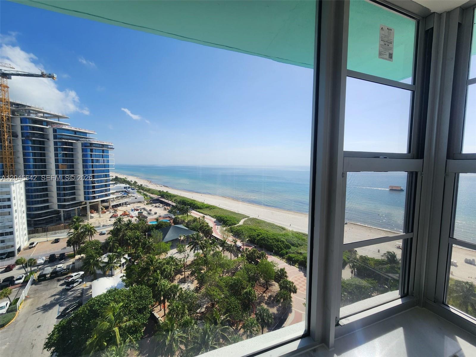 A high-angle view through a window shows a beach, ocean, and a nearby construction site — 5255 Collins Ave # 12E, Miami Beach FL 33140, MIAMI BEACH, FL