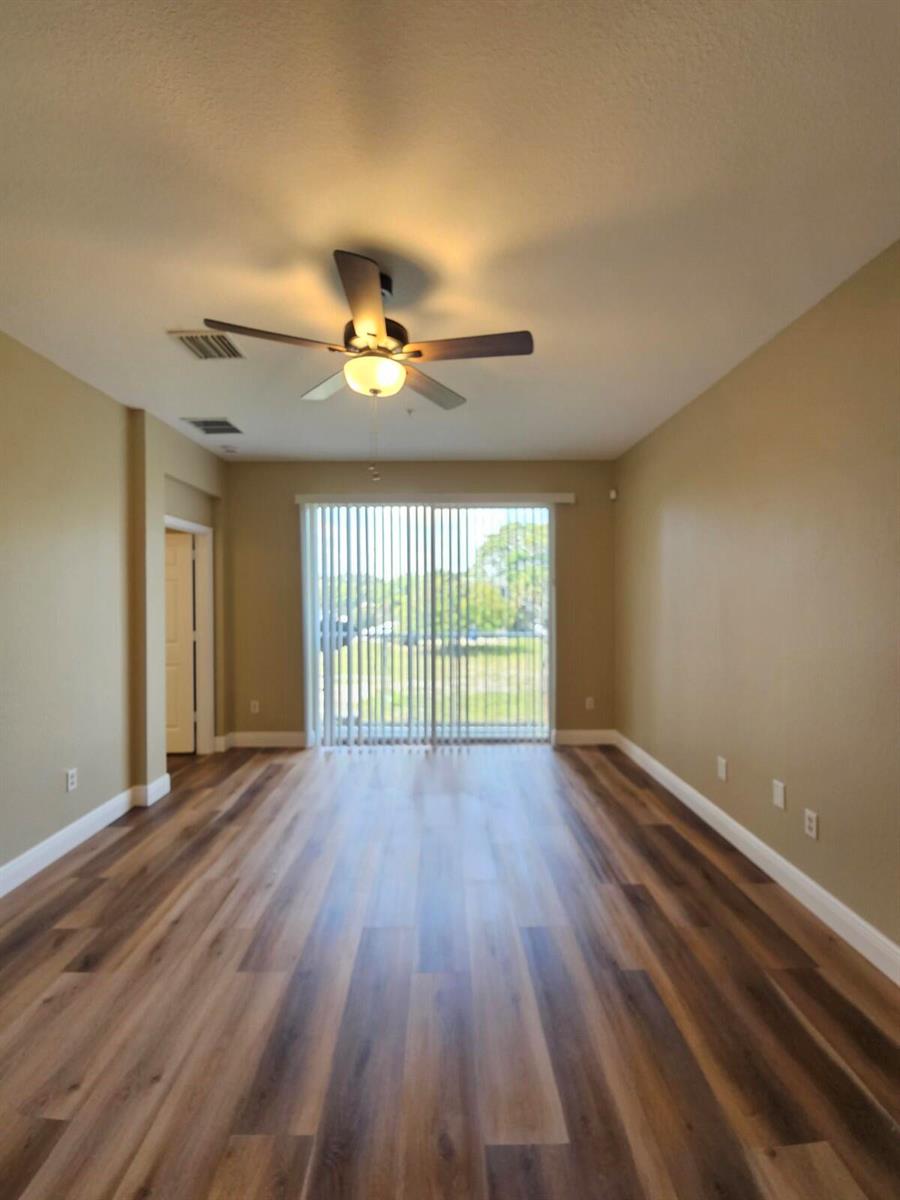 An empty living room features wood-look flooring, tan walls, a ceiling fan, and vertical blinds — 1979 Marsh Harbor Drive, Riviera Beach FL 33404, RIVIERA BEACH, FL