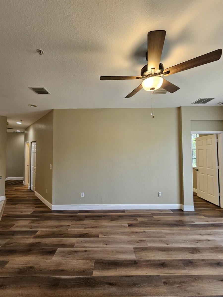 An empty room features wood-look flooring, beige walls, a ceiling fan, and two doorways — 1979 Marsh Harbor Drive, Riviera Beach FL 33404, RIVIERA BEACH, FL