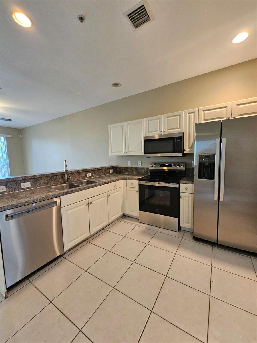 A kitchen features white cabinets, stainless steel appliances, granite countertops, and light-colored tile flooring — 1979 Marsh Harbor Drive, Riviera Beach FL 33404, RIVIERA BEACH, FL