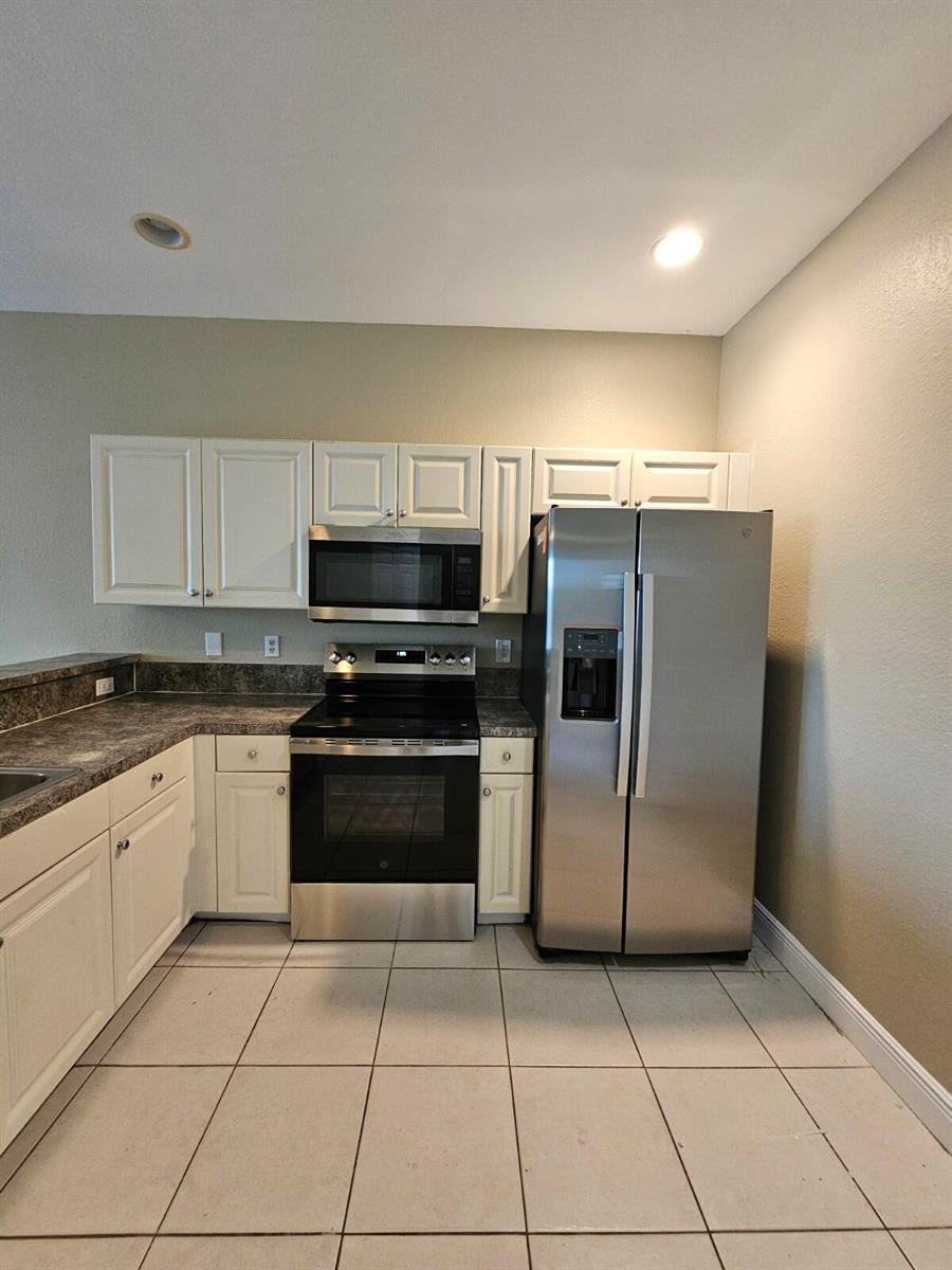 A kitchen features white cabinets, stainless steel appliances, dark countertops, and light tile flooring — 1979 Marsh Harbor Drive, Riviera Beach FL 33404, RIVIERA BEACH, FL