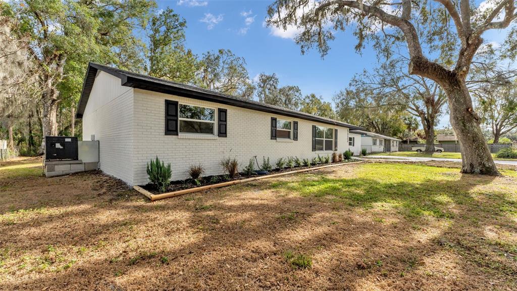 A white brick, single-story house with black shutters sits on a grassy lot with trees — 5322 FORESTBROOK DRIVE E, LAKELAND, FL