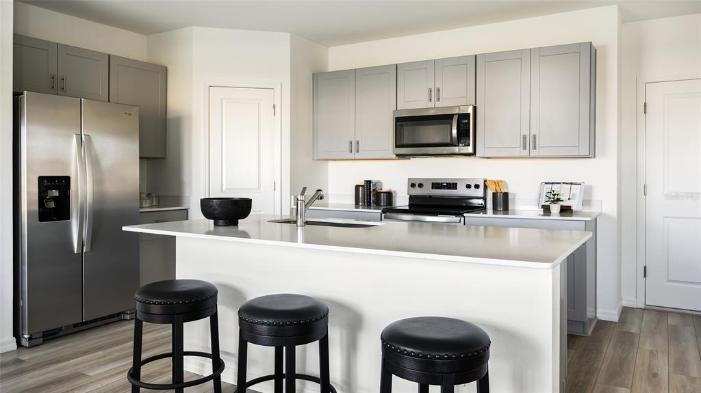 A modern kitchen features gray cabinets, stainless steel appliances, a white island, and bar stools — 4571 RIVERBEND BOULEVARD, HAINES CITY, FL