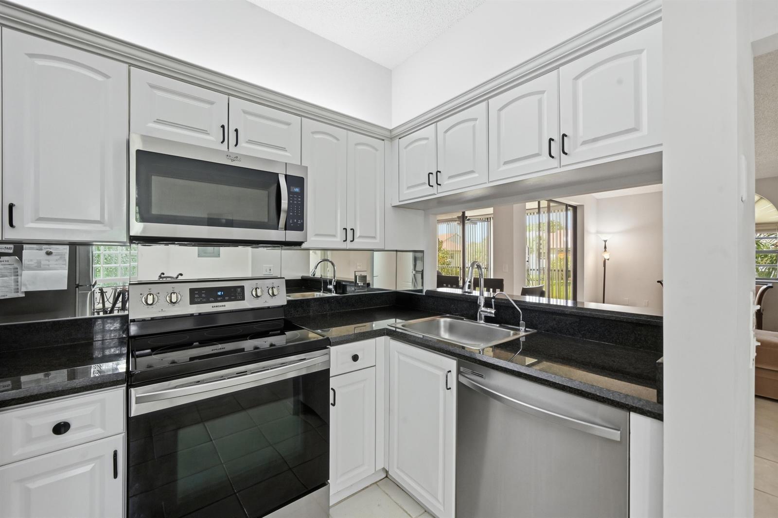 A kitchen features white cabinets, black granite countertops, stainless steel appliances, and a mirrored backsplash — 5395 Firenze Drive # K, Boynton Beach FL 33437, BOYNTON BEACH, FL