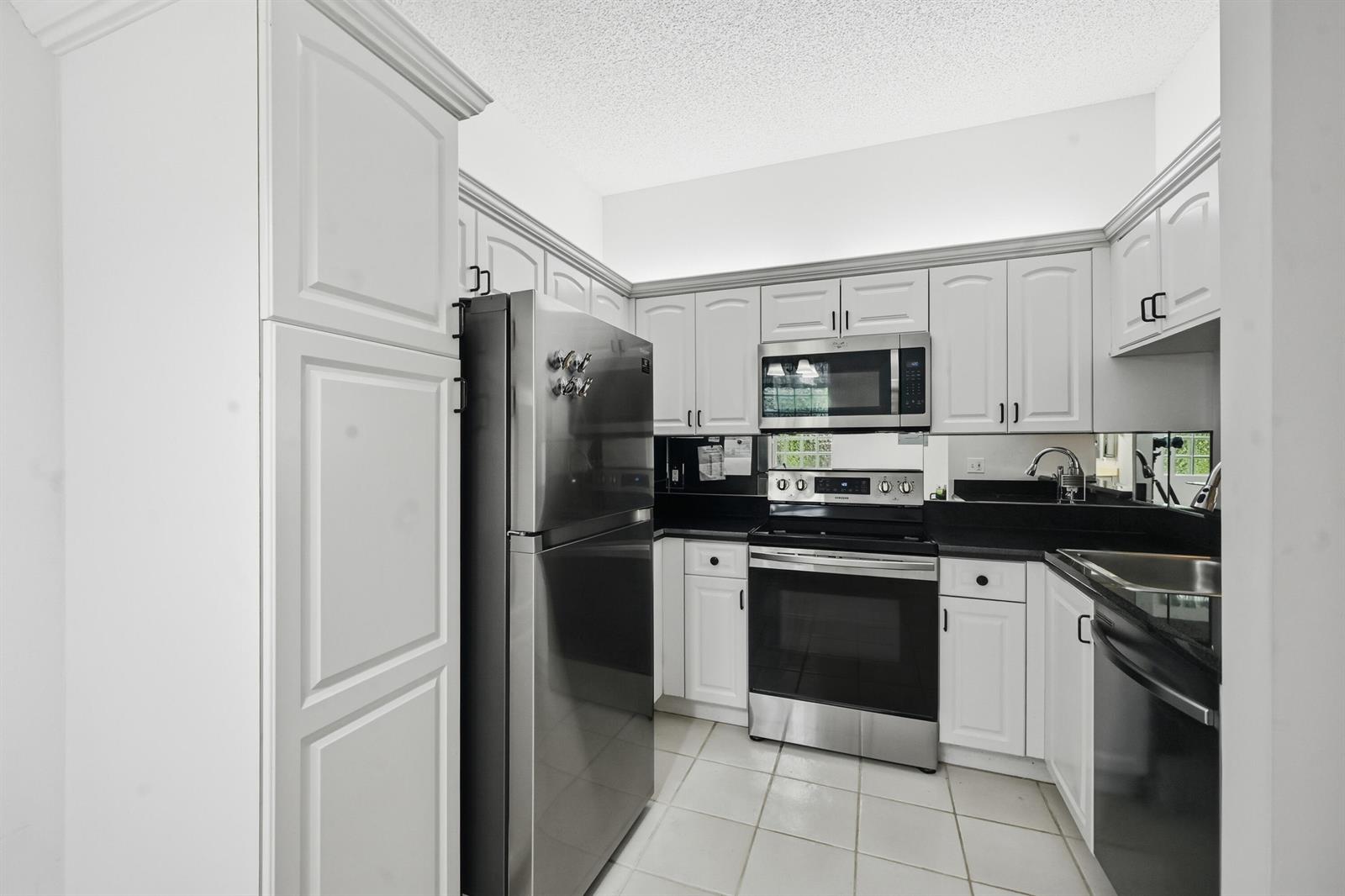 A kitchen with white cabinets, black countertops, stainless steel appliances, and light-colored tile flooring — 5395 Firenze Drive # K, Boynton Beach FL 33437, BOYNTON BEACH, FL
