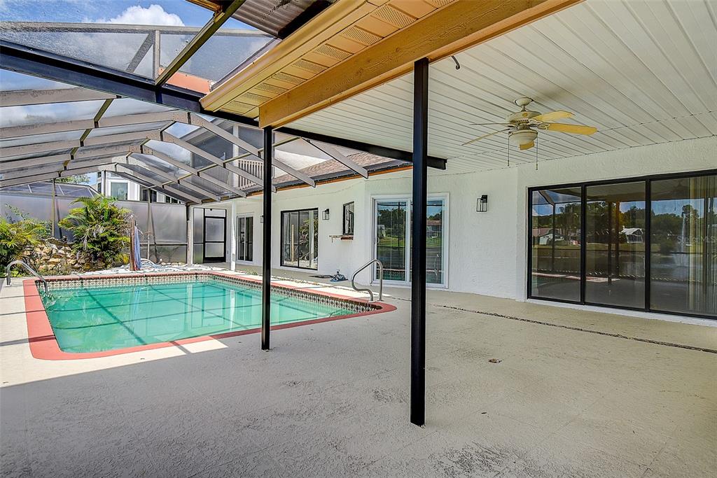 A screened-in pool enclosure with a concrete patio and a view of a pond — 2876 LAKE VALENCIA BOULEVARD E, PALM HARBOR, FL